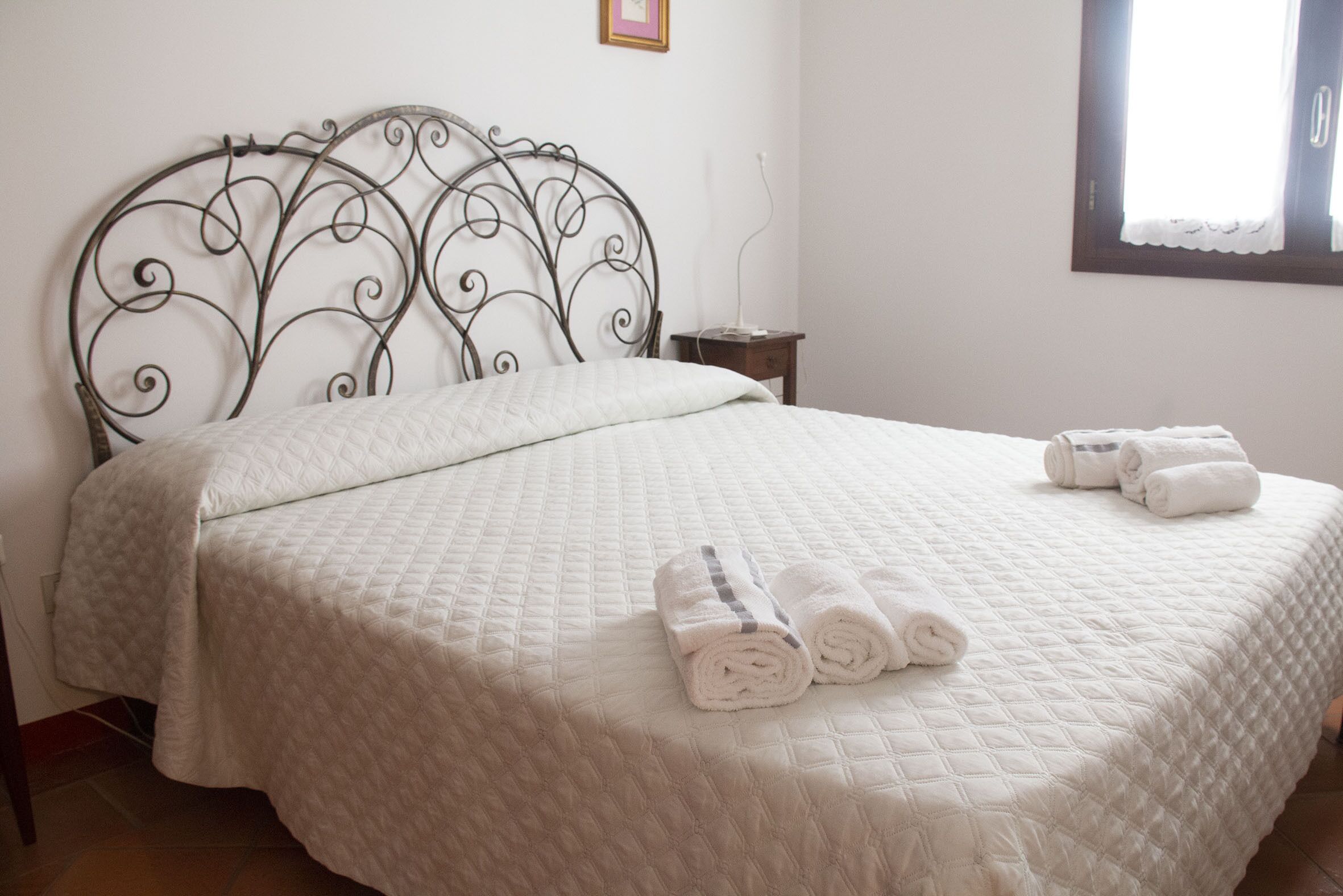 A neatly made bed with a quilted bedspread and rolled towels on the bed.