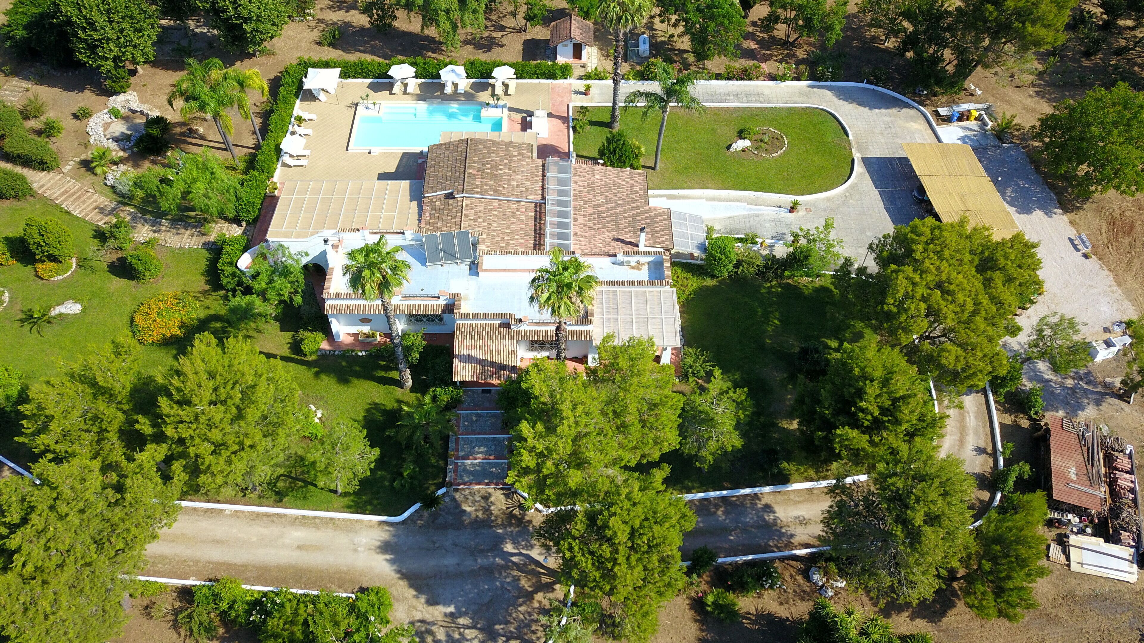 An aerial view of a residential property with a swimming pool, a covered patio, and a landscaped garden.