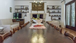 A dining room with a long wooden table, chairs, a white vase with fruits, and a fireplace. - Villa Vetti, beautiful villa surrounded by greenery with swimming pool, a few km from the sea (UGENTO)