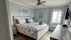 A bedroom with a bed, a ceiling fan, a nightstand, a dresser, and a window with curtains. - Clean Beautifully Remodeled Beachfront Condo (Myrtle Beach)