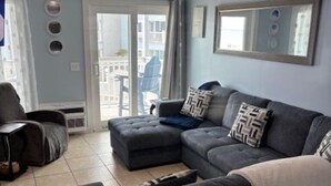 A living room with a grey sectional sofa, a white throw blanket, and a ceiling fan. - Clean Beautifully Remodeled Beachfront Condo (Myrtle Beach)