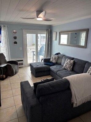 A living room with a grey sectional sofa, a white throw blanket, and a ceiling fan.