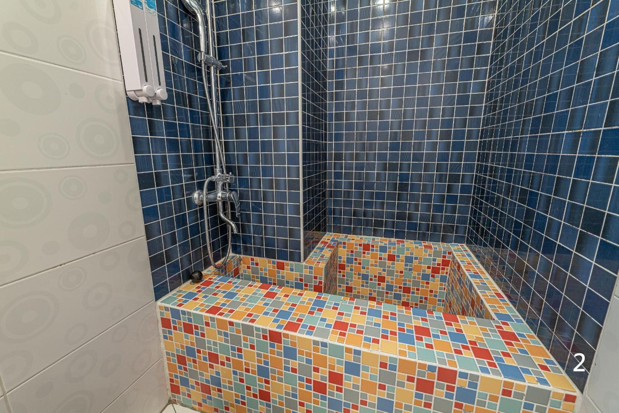 A shower area with blue tiles and a colorful mosaic floor.