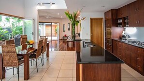 Una cocina moderna con una isla central, armarios de madera y un comedor con sillas de mimbre y una mesa de vidrio.