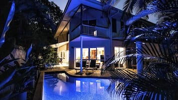 A two-story house with a swimming pool, a balcony, and a well-lit interior.