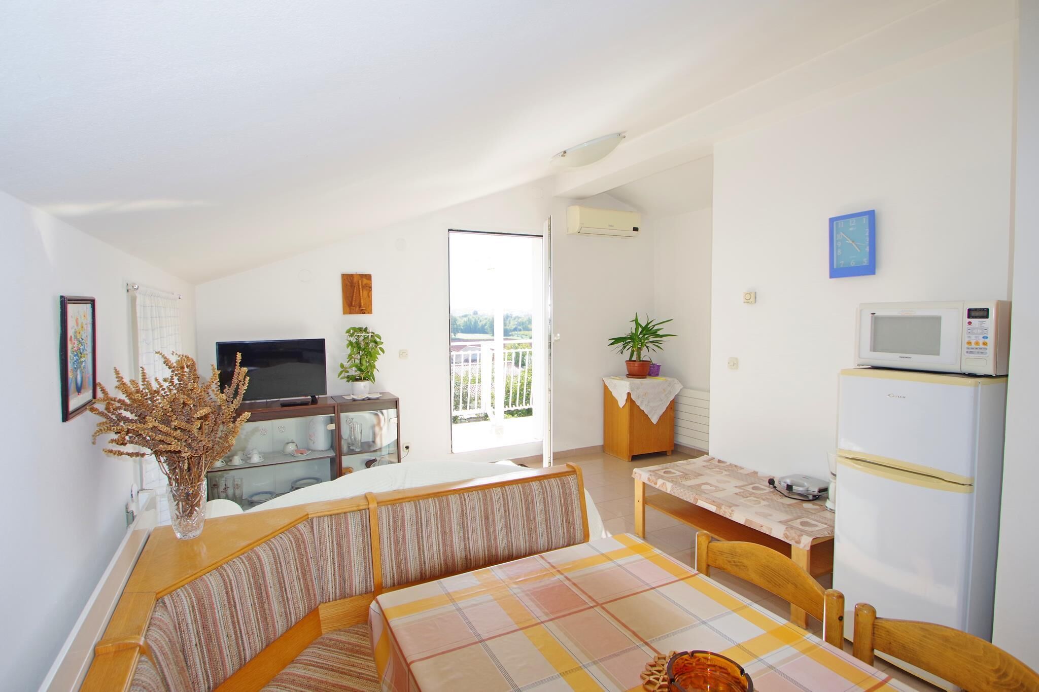 Un espacio habitable compacto con sofá, mesa de comedor, televisor, refrigerador y balcón con vistas.