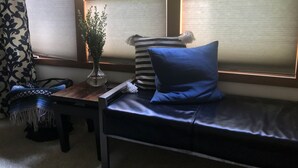 Una habitación con un asiento junto a la ventana, un jarrón con una planta, un cojín a rayas y una cortina estampada.