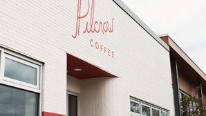 Un edificio con un letrero que dice "Pilcrow Coffee" en una fachada de ladrillo blanco con detalles rojos.