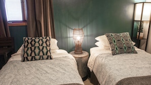 Una habitación con dos camas, cada una con almohadas estampadas, una lámpara de noche y una mesita redonda.