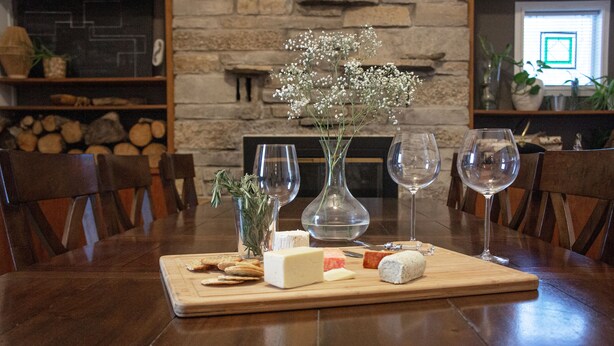 Una mesa de madera para comer con una tabla de quesos, copas de vino y un jarrón con flores.