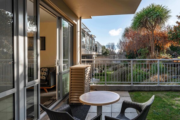 Ein Balkon mit Glastür, einem runden Tisch, Korbstühlen und einem Stapel Kissen.