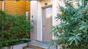 Een gebouw-ingang met een deur waarop '103' staat, een betonnen trap en omliggend groen.
