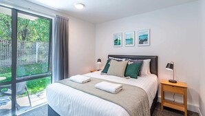 Een moderne hotelkamer met een groot bed, twee nachtkastjes, een raam met uitzicht op groen en twee ingelijste foto's aan de muur.