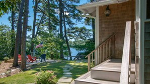 A wooden staircase leading to a covered porch with a view of a lake and trees. - Waterfront on Crystal Lake! (Orleans)
