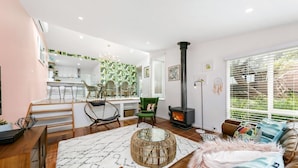 A modern living room with a fireplace, a dining area with a kitchen in the background, and large windows with blinds.
