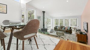 A modern interior with a dining area, a living space with a sofa and coffee table, and large windows providing natural light.