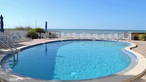 A pool with a clear view of the ocean, surrounded by lounge chairs and umbrellas. - Beachcomber unit 202 (Longboat Key)