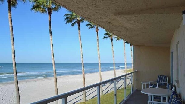 A balcony with a view of the beach and ocean, featuring a table and chairs. - Beachcomber unit 202 (Longboat Key)