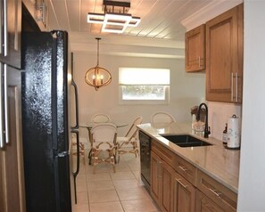 A kitchen with wooden cabinets, a black refrigerator, a chandelier, and a window providing natural light.