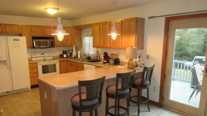 A kitchen with wooden cabinets, a central island with bar stools, a microwave, a stove, and a large sliding glass door leading to a balcony.