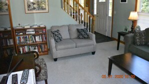 A living room with a grey sofa, a bookshelf, a coffee table, and a staircase.