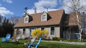A two-story house with a brown roof, a front porch, and a small garden with chairs.