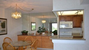 A modern kitchen with wooden cabinets, a built-in microwave, and a glass dining table with wicker chairs. - Beachcomber unit 501 (Longboat Key)