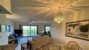 A modern living room with a glass dining table, sofas, and a ceiling fan. - Beachcomber unit 501 (Longboat Key)
