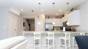 A modern kitchen with white cabinets, a central island with bar stools, and pendant lighting. - Four Bedrooms TownHome Close to Disney 5162A (Kissimmee)