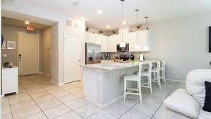 A modern kitchen with white cabinets, a central island with bar stools, stainless steel appliances, pendant lighting, and an exit sign. - Four Bedrooms TownHome Close to Disney 5162A (Kissimmee)