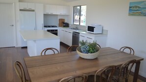 Cozinha compacta com armários brancos, micro-ondas e uma área de refeições com mesa e cadeiras de madeira.