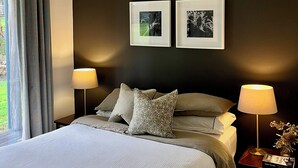 Quarto bem organizado com uma cama, duas mesas de cabeceira e duas fotografias emolduradas na parede.