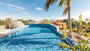 Piscina com azulejos de mosaico azul, cercada por palmeiras e edifícios.