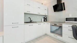 A modern kitchen with white cabinetry, a built-in oven, a microwave, and a black range hood. - Stylish Apartment with Gym | 400 m to the Beach, Balcony (Kolobrzeg)