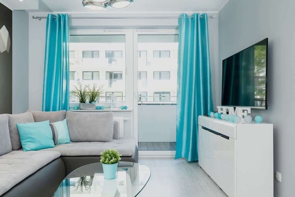 A modern living room with a sofa, a glass coffee table, and a TV mounted on the wall.