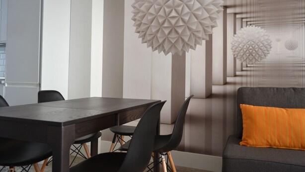 A modern dining area with a dark wooden table and black chairs, a gray sofa with an orange cushion, and a wall with geometric white decorations. - NEVERENDING RIJANA, Cala Rijana at your fingertips! (calahonda)