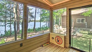 A wooden deck with large windows overlooking a lake, a paddleboard, and outdoor furniture. - Dock, Sauna & Hot Tub! 'Loon Lake Lodge' (Pequot Lakes)