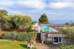 A stone house with a swimming pool, outdoor seating, and a staircase leading to a deck.