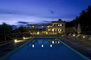 A swimming pool with a wooden deck and lounge chairs, surrounded by a wooden fence and a building with multiple windows.