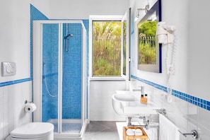 A bathroom with a shower, toilet, sink, and a window with a view of greenery.