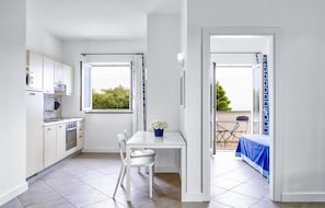 A modern kitchen with white cabinets, a dining table with chairs, and a view through an open door to an outdoor seating area.