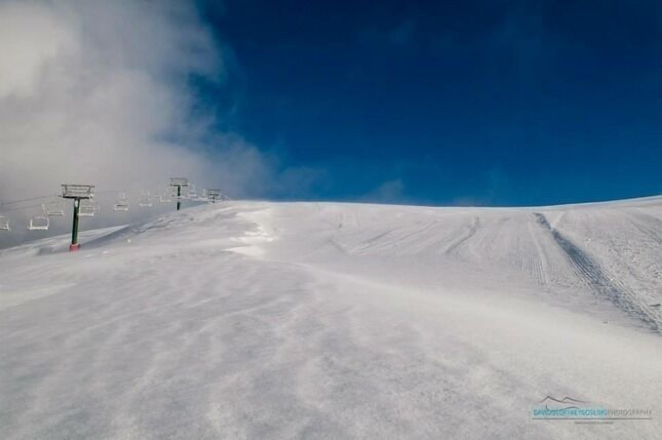 A snowy ski slope with ski lifts and a clear blue sky.