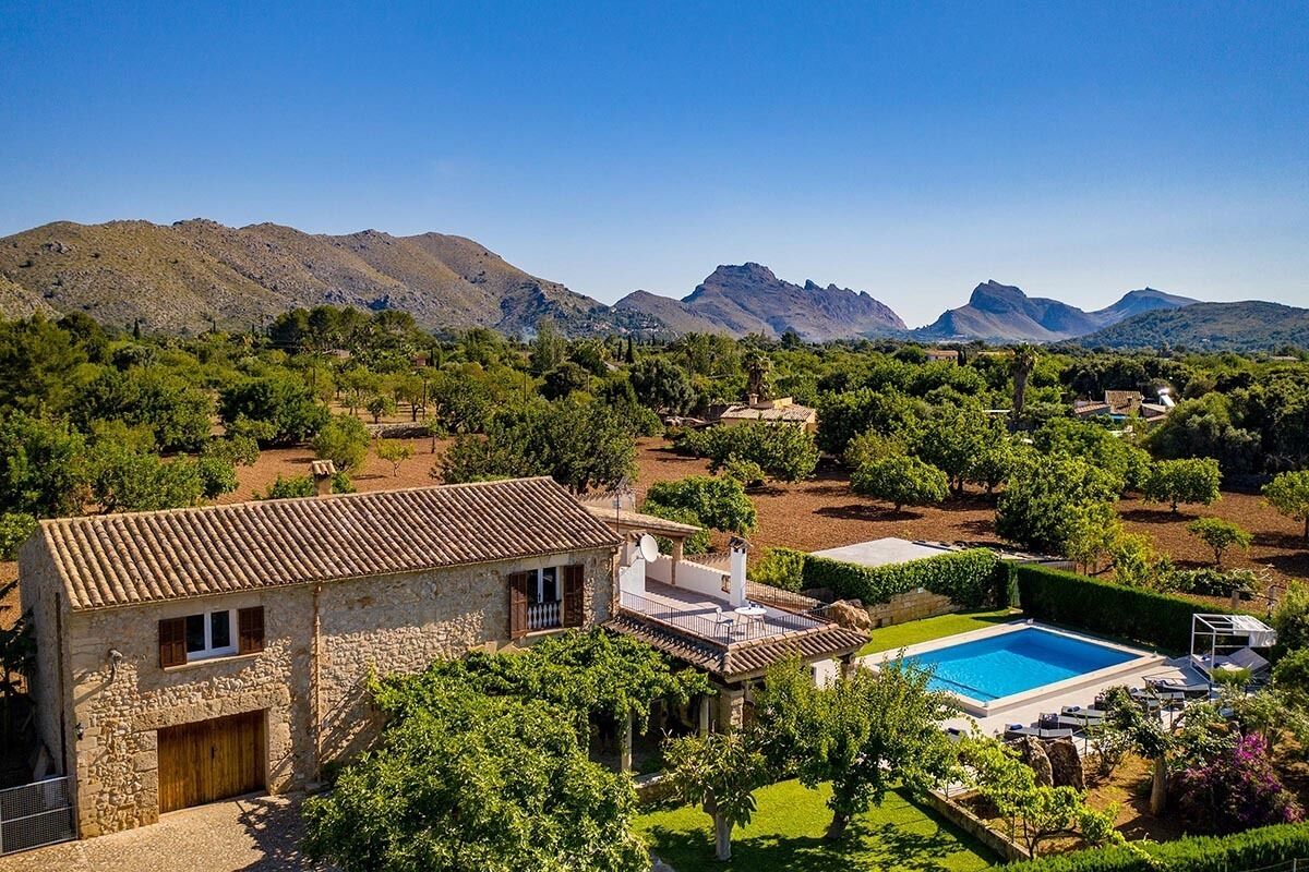 A stone villa with a swimming pool, surrounded by lush greenery and mountains in the background.