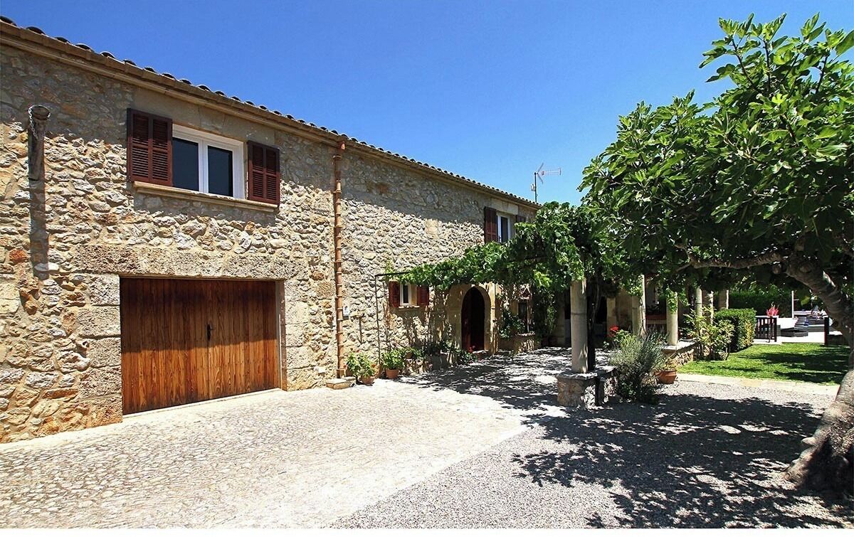 A stone building with a wooden door and windows, a gravel courtyard, and a tree.