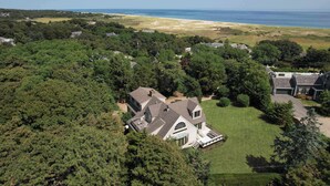 An aerial view of a large house surrounded by dense trees, with a beach and ocean in the background. - Private Beach and Roof Top Deck! (Orleans)
