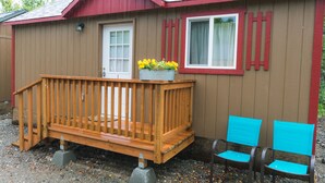 A wooden deck with a planter of yellow flowers, a door, and a window with a curtain.