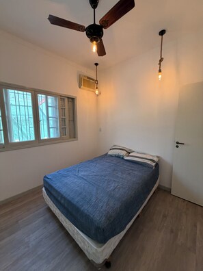 Une chambre à coucher avec un lit, un ventilateur de plafond, une fenêtre et une porte.