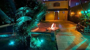 A courtyard with a fire pit, palm trees, and a building with a yellow facade. - HOUSE WITH POOL CANTO DO FORTE, 10 people (Praia Grande)