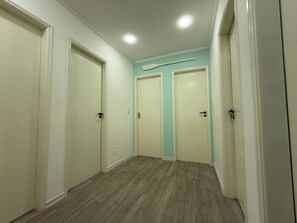 Un couloir avec trois portes, un plancher en bois et un luminaire au plafond.