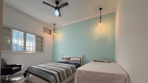 Un dormitorio con dos camas, ventilador de techo, ventana con persianas y una silla.